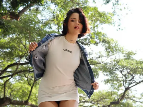 LaurenWard — Young woman in a white t-shirt and denim jacket standing under lush green trees in bright sunlight.