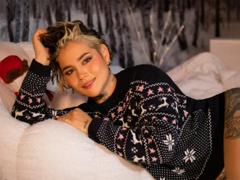LaurenWard — Smiling woman in a black patterned Fair Isle sweater relaxing on white bedding in a cozy indoor setting.