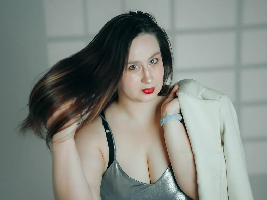 Young woman with long brown hair in a silver top posing in a bright studio setting.