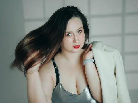 LatteaViia — Portrait of a woman in a silver top and white blazer with long brunette hair in a bright studio setting.