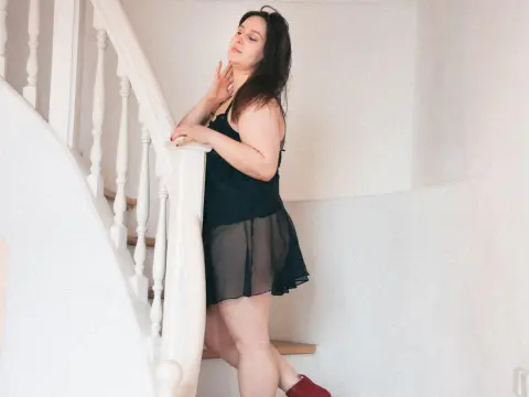 LatteaViia — Woman in a black slip dress leaning against a white staircase in a bright, minimalist indoor setting.