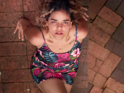 KatalinaCruz — Young woman in a floral print sundress lying on a rustic brick patio in soft natural light.