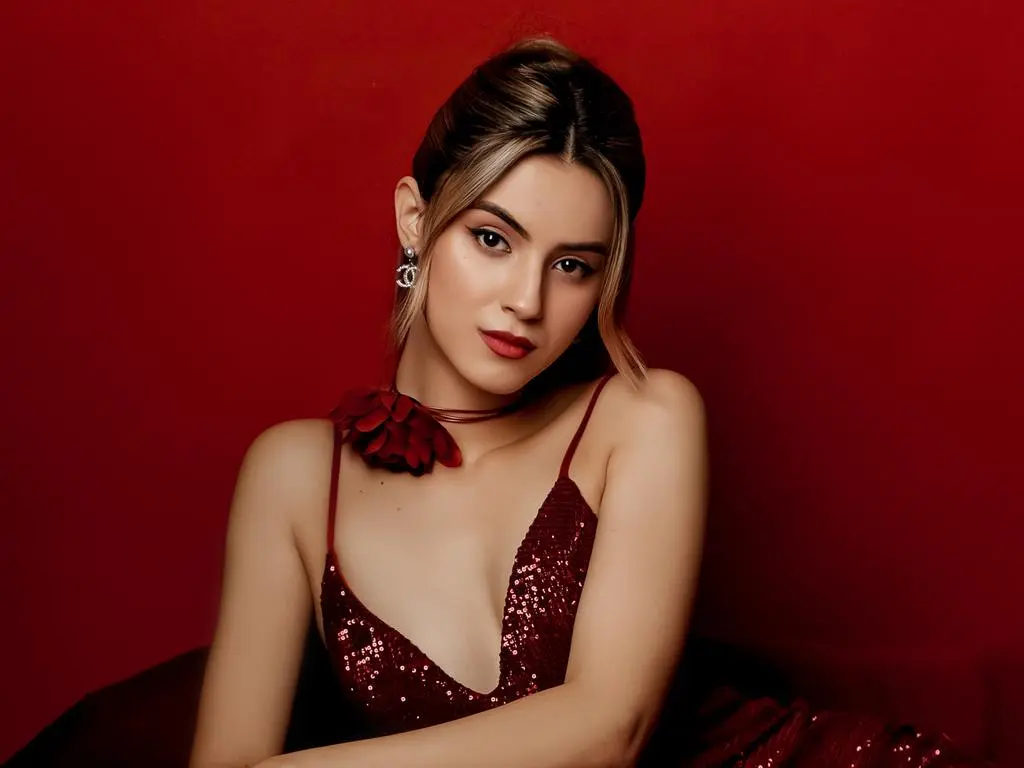 JasmineLove — JasmineLove poses in a sparkly red dress and flower choker against a red background.