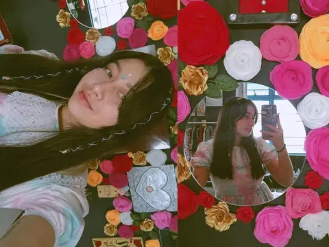 Andromeda_ — Young woman in a white lace top posing in front of a romantic floral heart mirror decoration.