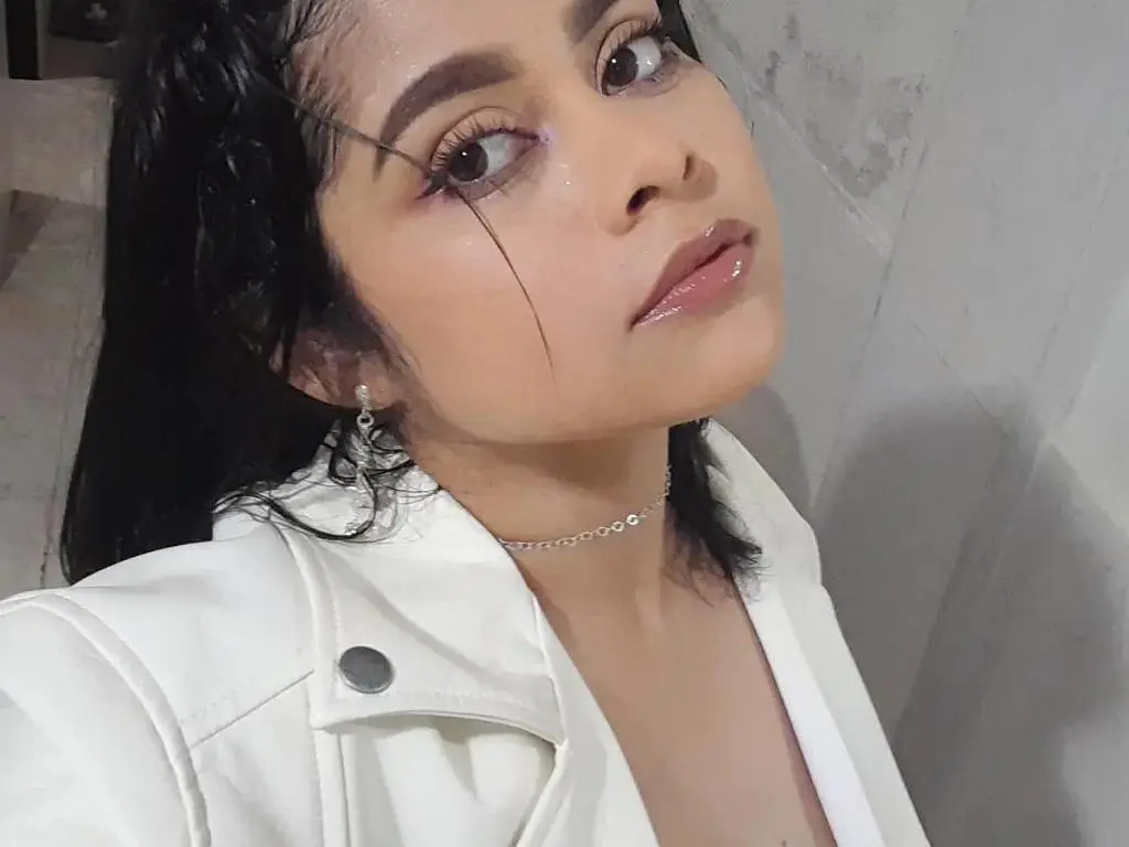 Lili_Nord poses in a white jacket and silver choker, looking at the camera with wet, dark hair and glossy lips.