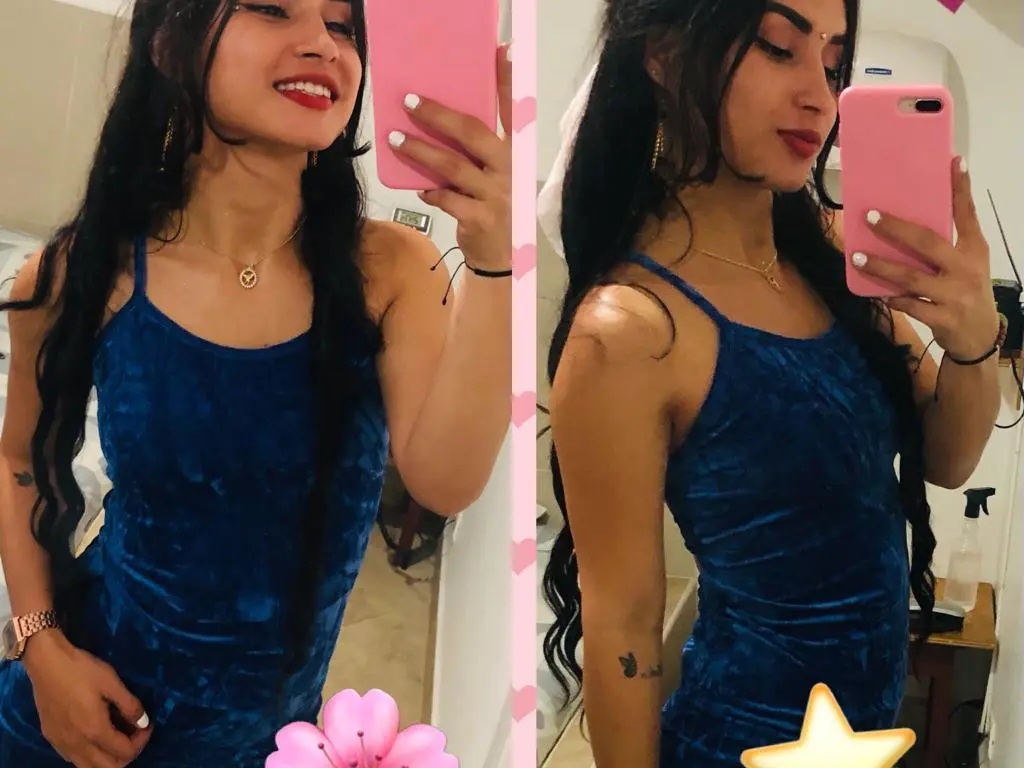 NadiaRoden — Young woman in a blue velvet dress taking a mirror selfie in a bright room.