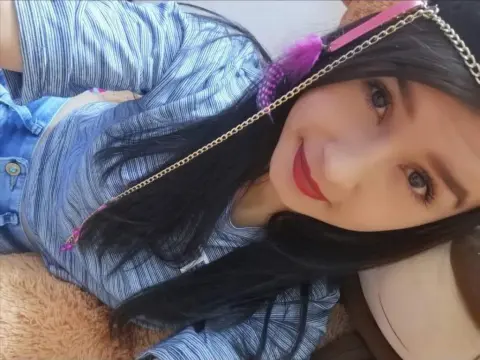 Smiling young woman with long dark hair wearing a blue striped shirt and pink headband relaxing indoors.