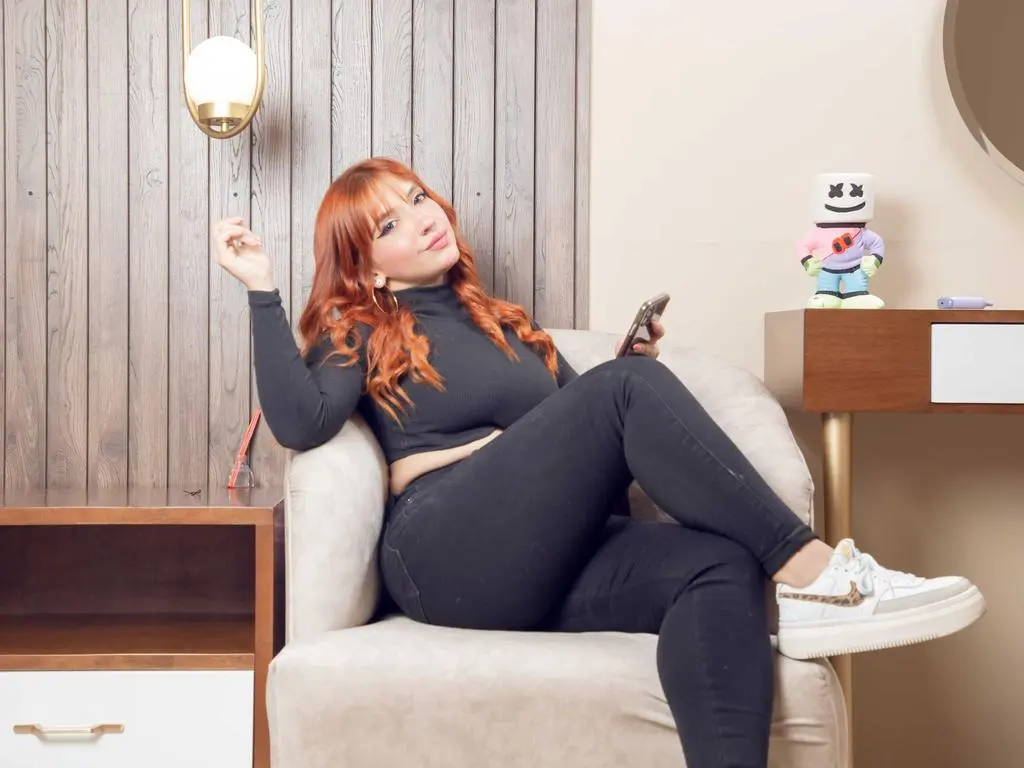 Sweet_Sandy — Redheaded woman in a black turtleneck and jeans relaxing in a modern armchair with a smartphone.