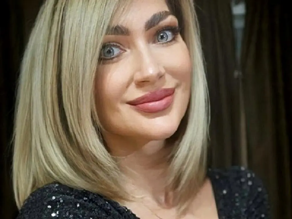 MilaIsHott — Smiling blonde woman in a black sequin dress posing for a glamorous portrait.