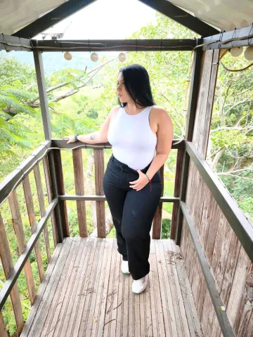QueenSofia — QueenSofia stands on a wooden balcony wearing a white tank top and black pants.