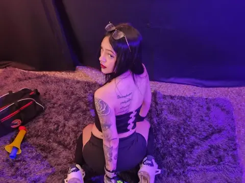 violetta575 — violetta575 sits on a purple shag rug wearing a black crop top and leggings, looking back over her shoulder with sunglasses on her head.