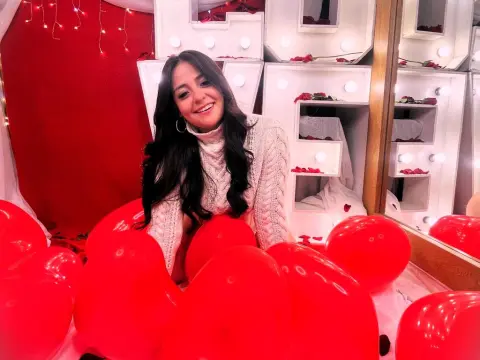 SamanthaClay — Smiling woman in a white knit sweater sitting among red balloons in a festive, romantic setting.