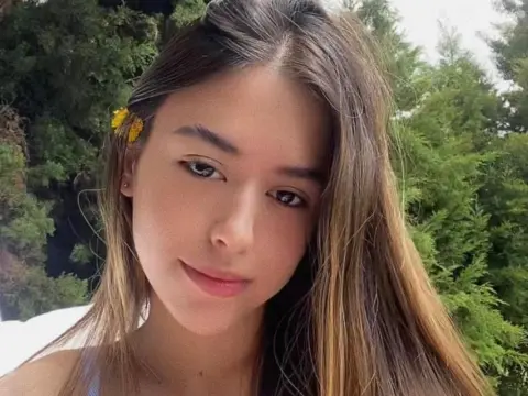Young woman with long brown hair and a yellow flower accessory smiling in a lush green outdoor setting.