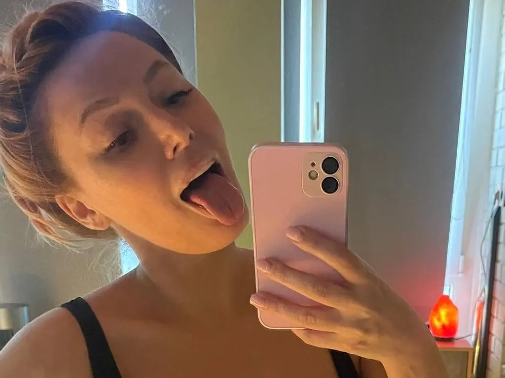 LoveCall — Playful young woman in a black tank top taking a cheeky mirror selfie with a pink smartphone.