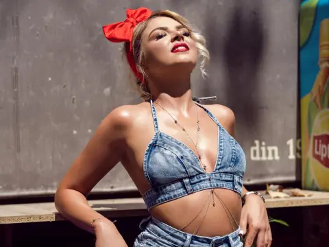 KimmyBliss — Blonde woman in denim halter top and red hair bow posing outdoors in sunny retro style.