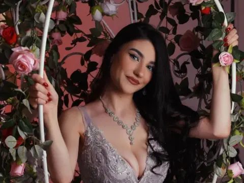 NorraJoice — NorraJoice smiles while wearing a silver sequined dress and a diamond necklace, posing inside a floral arch.