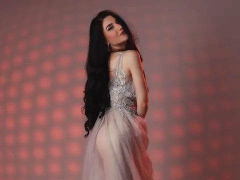 NorraJoice — NorraJoice poses in a sheer grey lace dress with long dark hair against a red patterned background.