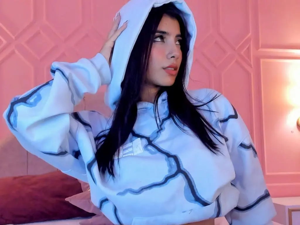 NaomyAshe_ — Young woman in a white oversized hoodie relaxing in a cozy pink bedroom setting.