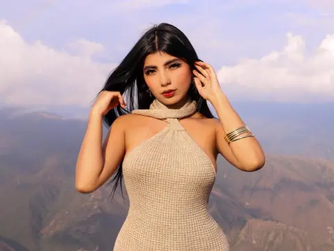 NaomyAshe_ — Young woman in a beige knit halter top posing against a scenic mountain landscape under a soft sky.