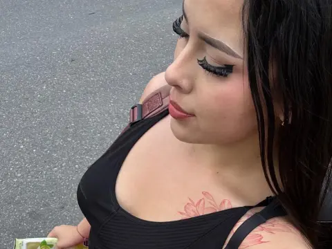 Alison_Tatcher — Young woman with long dark hair and floral tattoo wearing a black tank top outdoors on a cloudy day.