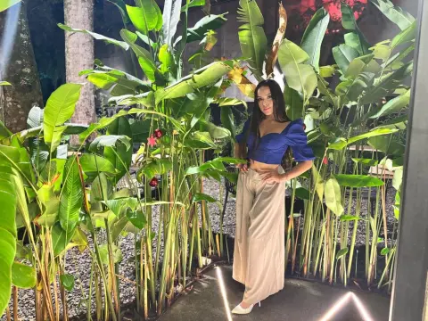 Alison_Tatcher — Stylish woman in a blue puff-sleeve crop top and beige wide-leg trousers posing in a lush tropical garden.