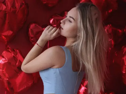 MargoCroftoon — MargoCroftoon poses in profile wearing a light blue tank top against a background of red heart-shaped balloons, running her hand near her mouth.