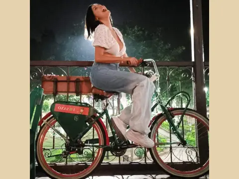 Mix_Kitty — Joyful woman in white blouse and jeans riding a vintage green bicycle at night.