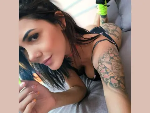 Mix_Kitty — Tattooed woman in a black tank top relaxing on a sofa with a serene expression.