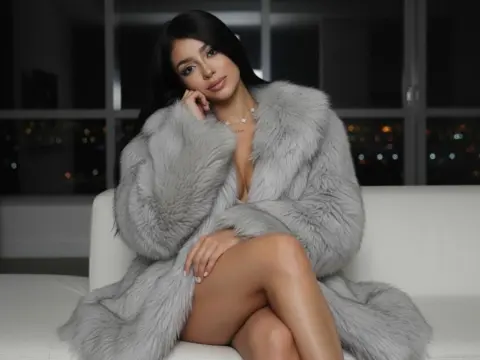 Shantal_Turner — Elegant woman in a grey faux fur coat sitting on a white sofa in a luxury nighttime penthouse setting.