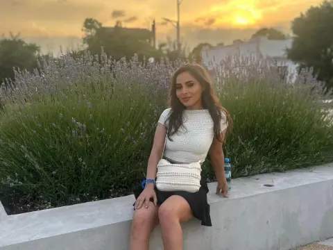 SarahSkye895 — Woman in white knit top and black skirt sitting by lavender bushes during a golden sunset.