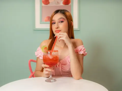 Young woman in a pink ruffled top sipping a refreshing red cocktail at a mint green cafe table.