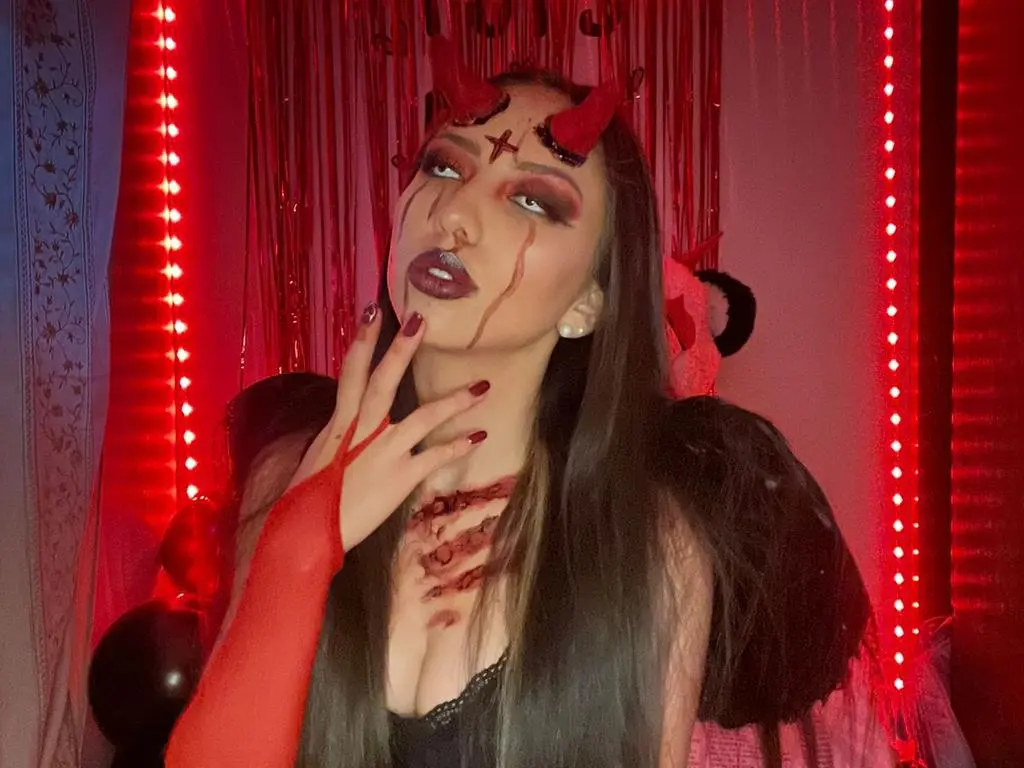 AriaFoxx — Woman in dark devil cosplay with red lighting and dramatic makeup in a spooky setting.