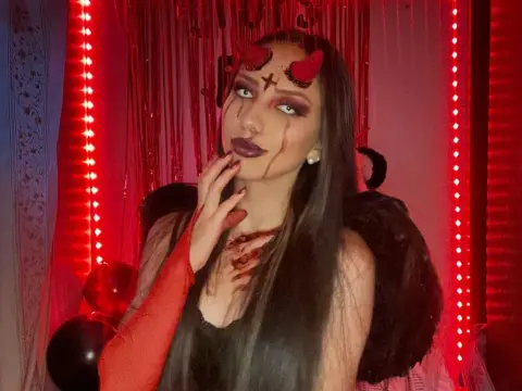 AriaFoxx — Woman in a dark devil costume with red horns and dramatic makeup posing against red tinsel decor.