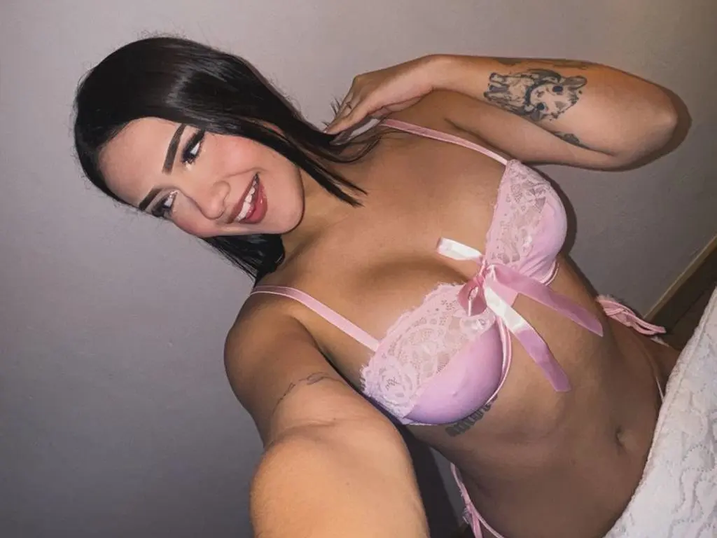 Smiling young woman in pink lace lingerie posing indoors for a playful selfie.