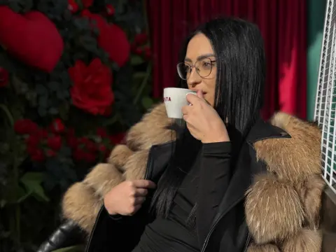 Stylish woman in black outfit and fur coat sipping coffee in a romantic rose garden setting.