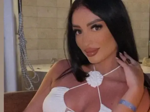 Smiling woman in a white halter neck top posing in a bright, modern indoor setting.