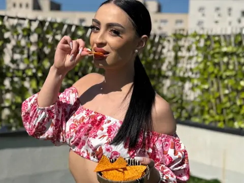 Young woman in floral off-the-shoulder top eating tortilla chips on a sunny outdoor patio.