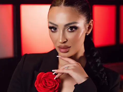 Glamorous woman in a black blazer with a red rose detail posing against a red studio background.