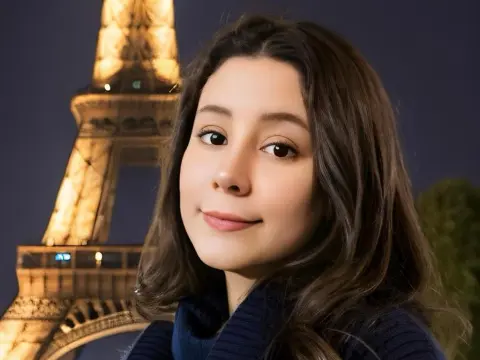SweetTulip — Smiling young woman in a navy sweater posing in front of the illuminated Eiffel Tower at night.