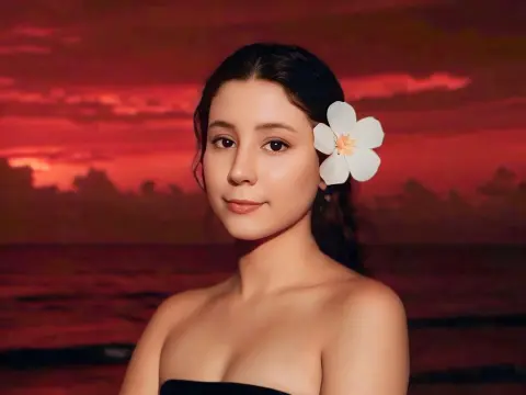 SweetTulip — Young woman with a white flower in her hair posing against a dramatic red sunset ocean backdrop.