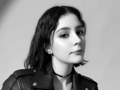 SweetTulip — Portrait of a young woman with wavy hair wearing a black leather jacket and choker in a minimalist studio setting.