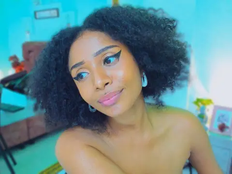 Megan_Wlliams — Young woman with curly hair and winged eyeliner posing in a bright blue room.