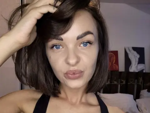 AvaCarterr — Close-up portrait of a young woman with brown hair and blue eyes posing in a cozy bedroom setting.