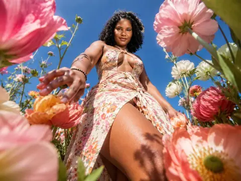 Woman in floral maxi dress standing in a sunny pink flower field under a blue sky.