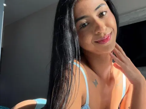 Smiling young woman with long dark hair in a light blue camisole enjoying warm sunlight indoors.
