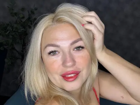 HelenOneLove is a blonde woman with red lipstick smiling and running her hand through her hair.