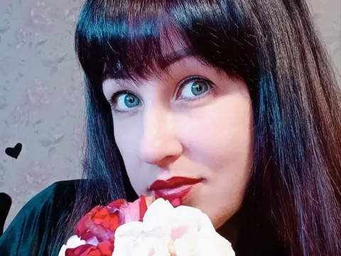 Portrait of a woman with dark bangs and blue eyes holding pink and white flowers in a soft, romantic mood.