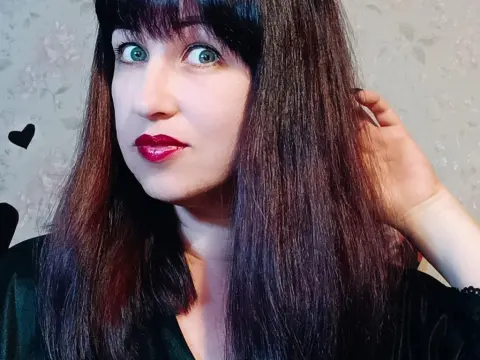Woman with long dark hair and red lipstick wearing a black top in a cozy indoor setting.
