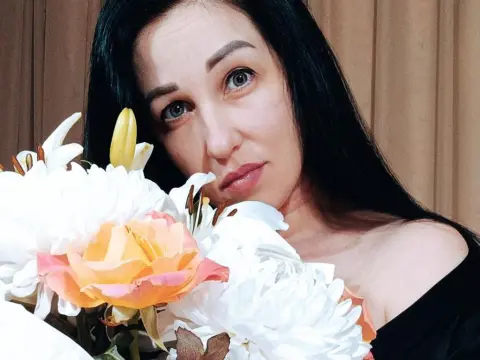 Beautiful woman with long black hair holding a bouquet of white and peach lilies in a soft indoor setting.