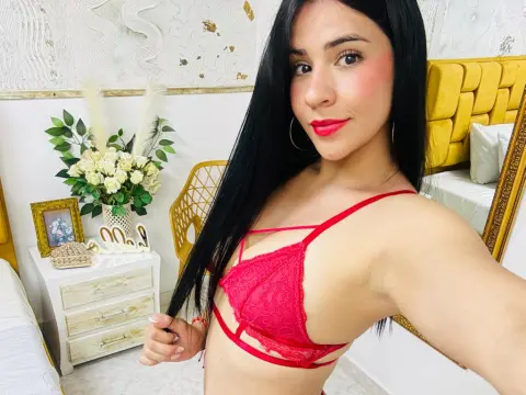 Amaia_Cooper — Smiling young woman with long black hair in red lace lingerie relaxing in a bright, modern bedroom.